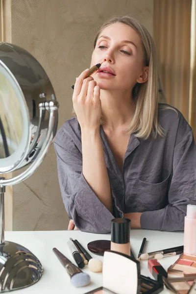 鏡を見る美しいブロンドの女性は コンシーラーと補正器 ファンデーションを使用して 化粧をします ホームインテリア — ストック写真