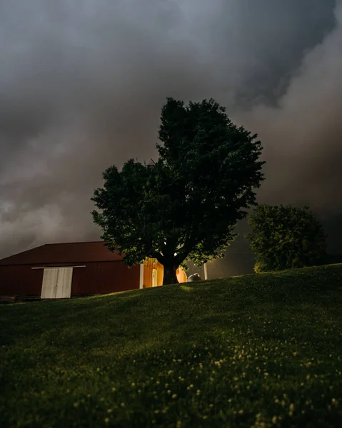 暗い曇りの空の背景に緑の木々の後ろの丘の上の小さな家の低角度ショット — ストック写真