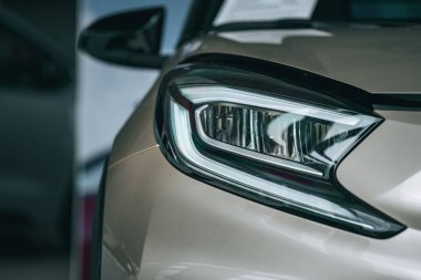 Beyaz bir arabanın ön kısmının yakın çekimi ve küçük yağmur damlaları olan far.