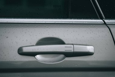 Gri bir otomobil kapısının yakın plan resmi. Taze yağmur damlalarıyla kiraz kolunun sapı.