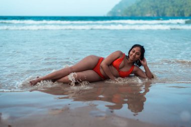 Turuncu bikinili güzel kadın kumlu sahilde denize karşı yatıyor..