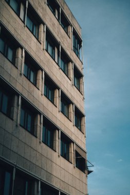 Mavi gökyüzünün altında koyu renkli pencereleri olan eski bir taş binanın dikey alçak açısı