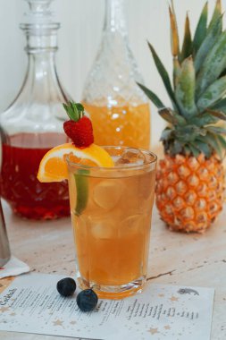 Meyve ve ve cam şişelerle dolu masada taze sıvı bulunan dikey yakın plan bir shot bardağı.