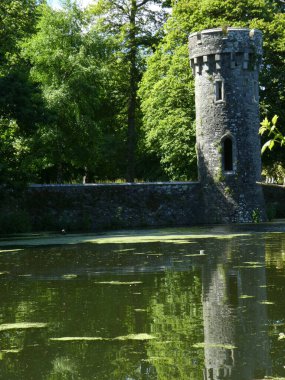 Bir gölete yansıyan taş kule ve duvarın dikey görüntüsü.