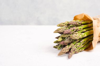 Beyaz dokulu bir masada taze yeşil kuşkonmaz, baharda sebzeler, gurme yemekleri, vejetaryen yemeği.