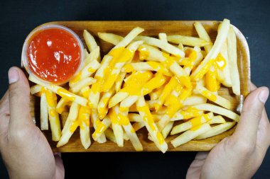 Koyu arkaplanda soslu patates kızartması tutan ellerin üst görüntüsü