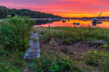 Gün batımında teknelerle dolu bir gölün arka planında çimenlerin üzerinde yürüme yolunun güzel bir görüntüsü..