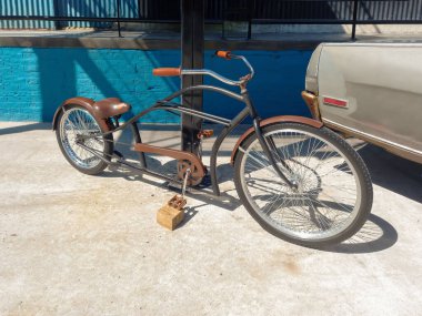 Metal bir direğe yaslanmış eski kahverengi bir bisiklet.