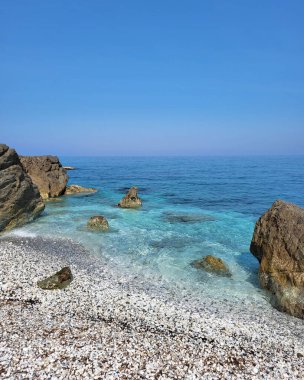 Gökyüzü arka planında kayalar olan mavi bir okyanusun dikey görüntüsü