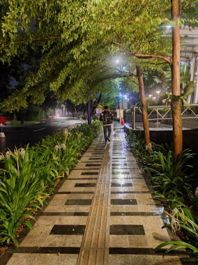 Gece ışıklarında parlayan binaların arka planındaki fayanslı yürüyüş yolunun dikey çekimi..