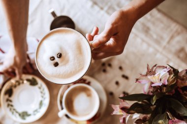Çiçeklerin arka planında bir fincan kahvenin üst görüntüsü.