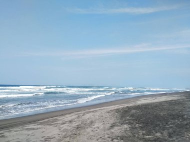 Okyanus dalgalarının kumlu bir sahile vurduğu sakin bir manzara.