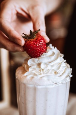 Bir elin dikey yakın çekimi milkshake 'e çilek ekliyor.