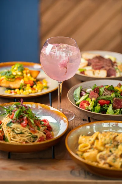 意大利面和沙拉的垂直特写 盘子里有蔬菜和肉片 还有一杯鸡尾酒 — 图库照片