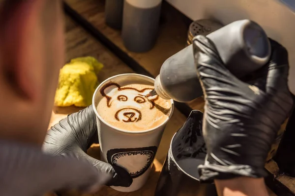 A closeup shot of a barista drawing a bear\'s head on a coffee