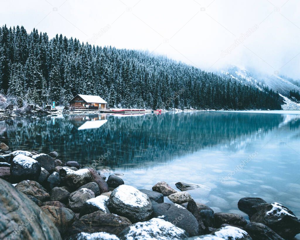 A view of the Moraine Lake in winter with a house and pine trees near in Banff National Park