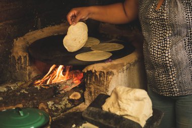 Meksika 'lı bir kadının mısır hamuru ile bir meta ve ahşap soba üzerinde çalışarak tortilla yapmasını izlemek.