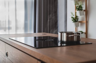 Mutfakta ahşap yüzeyi olan metal bir tencereyle parlak, siyah, modern bir fırının güzel bir iç çekimi.