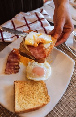 Kahvaltıda yumurta ve pastırmalı sandviç yapan birinin dikey yakın çekimi.
