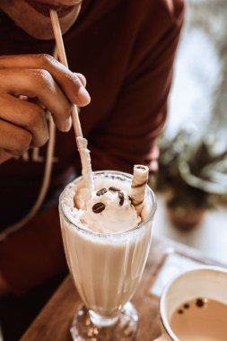 Kahve çekirdeği ve kurabiyeyle milkshake içen birinin dikey yakın çekimi.