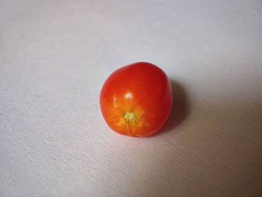 Beyaz bir yüzey üzerinde kırmızı bir vişne domatesi.
