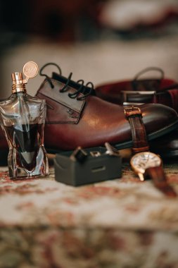 Kol saati ve parfümü düğüne hazır erkek kahverengi deri ayakkabılarının dikey yakın çekimi.