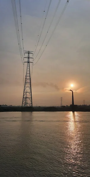 Vertikální Záběr Vysílací Věže Dálce Břehu Řeky Pozadí Západu Slunce — Stock fotografie