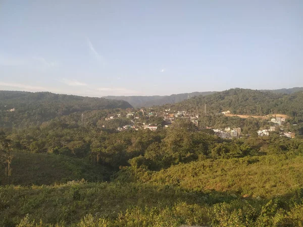 晴れた日には鬱蒼とした緑に覆われた丘に囲まれた町の高い角度のショット — ストック写真