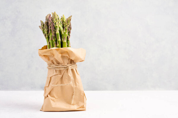Свежая зеленая связка спаржи на белом текстурированном столе, овощи весной, изысканная кухня, приготовление веганской еды
