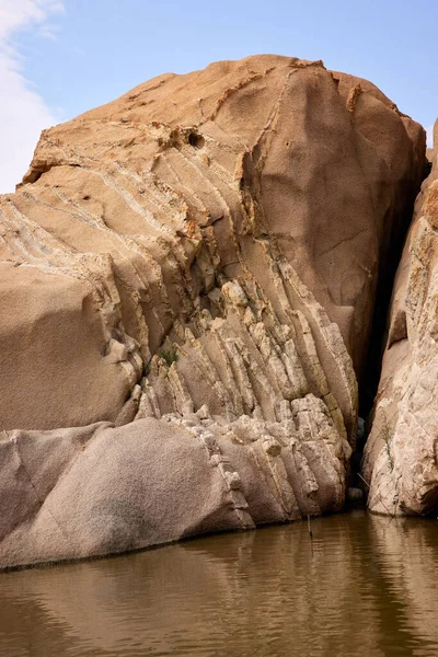 Güneşli bir günde çöldeki sakin bir gölün üzerinde yükselen yüksek ve kayalık uçurumların dikey görüntüsü.