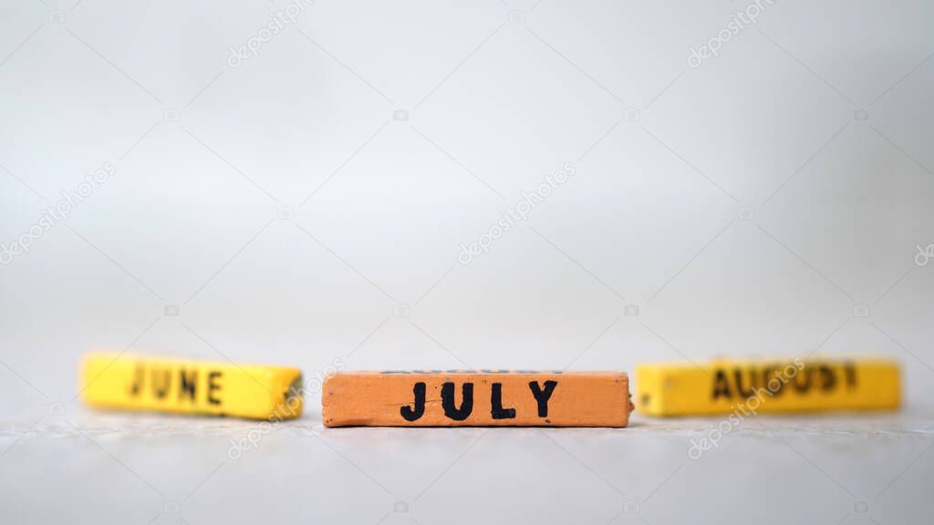 A close-up shot of three wooden blocks of months of the summer.