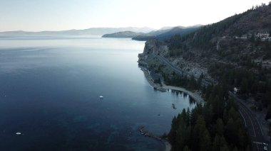 Amerika 'nın Tahoe Gölü' nün batı kıyı şeridi boyunca kuzeye bakan sisli bir sabahın dramatik drone görüntüsü.
