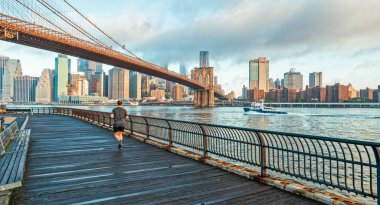 Genç bir adam Brooklyn Köprüsü 'nün altında köprüde koşuyor. New York CIty Skyline ile.