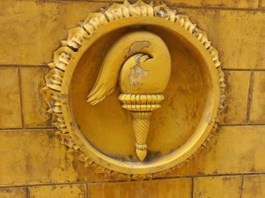Sarı tuğla duvarda daire şeklinde çerçeveli meşale heykeli..
