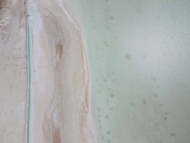 Okyanusun sakin suyunun ve kumlu kumsalın hava aracı görüntüsü.