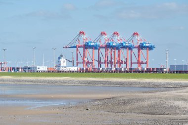 Gantry vinçleri, Almanya 'nın Wadden Denizi ve gelgitlerle çevrili bir endüstriyel kargo limanına konteynır yüklüyor..