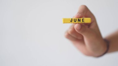 Beyaz arka planda Haziran ayının bir bloğunu tutan bir elin yakın plan çekimi..