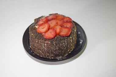 Beyaz arka planda çilek dilimleri olan küçük bir çikolatalı pasta.