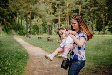 Küçük kızıyla birlikte ormanın yakınındaki bir parkta yürüyüş yapan güzel ve genç bir kızın yakın çekimi.
