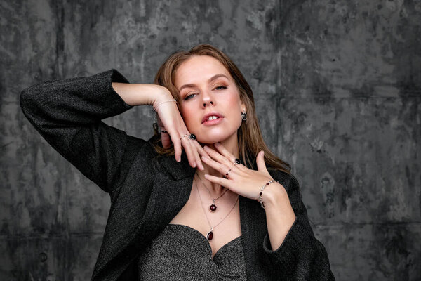 A Caucasian girl posing in the studio with hands under her face with a dark outfit and jewelry