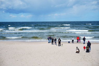 Kumsalın manzarası ve deniz kenarında duran bir grup insan.