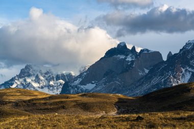 Şili 'deki Torres del Paine Ulusal Parkı' nda bulutlu bir gökyüzüne karşı karla kaplı kayalık dağlar.