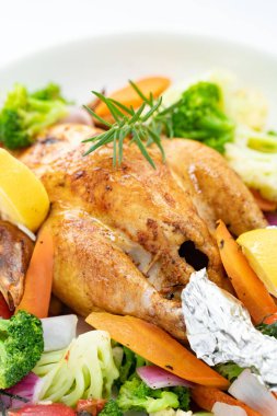 Kızarmış tavuğun beyaz tabakta sebzeli dikey görüntüsü.