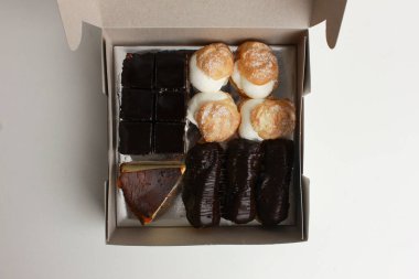 Beyaz bir kutudaki keklerin, eklerlerin, çikolatalı keklerin ve peynirli keklerin üst görüntüsü. Lezzetli tatlı lezzeti.