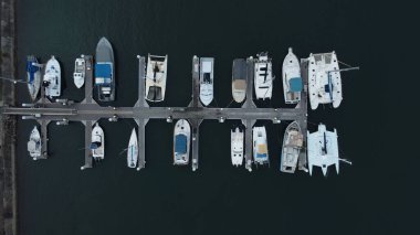 Rıhtımda sakin bir suya park edilmiş teknelerin hava görüntüsü.