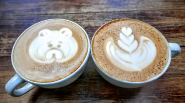 Ahşap bir masaya köpük çizilmiş iki fincan kahvenin açısı..