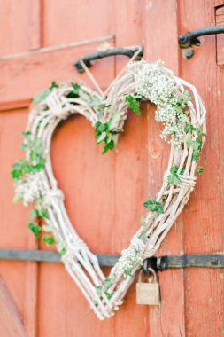 Kırmızı ahşap bir kapının üzerinde klasik bir kırsal kalp dekorasyonunun dikey görüntüsü.