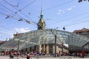 İsviçre, Bern 'de modern cam çatılı ve saat kulesi olan tren istasyonunda bir sürü insanın yürüdüğü bir cadde.