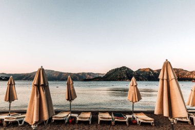 Kapalı plaj şemsiyeleri ve deniz kenarında boş plaj yatakları. Gün batımında gökyüzünün altında uçurumlar.