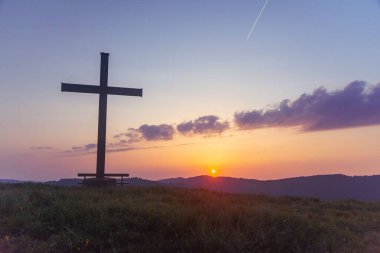 Tarladaki tepeden gün batımının altın rengi manzarasındaki haç.